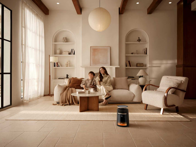 A DREO heater placed on a rug in a living room, where a woman and a young boy sit together on a sofa.