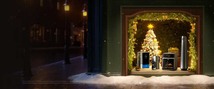 Decorative display of a Christmas tree and electronic devices in a window with a snowy street outside.